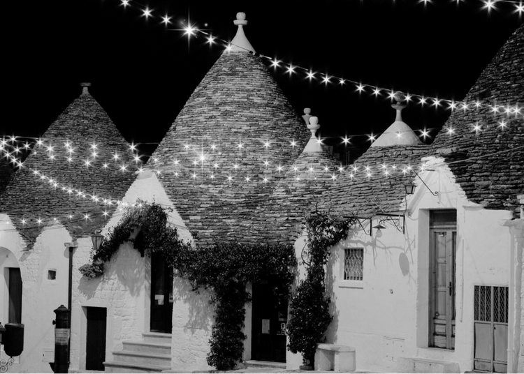 Promotional flyer for 'Christmas in July' event with Trulli architecture and festive lights.